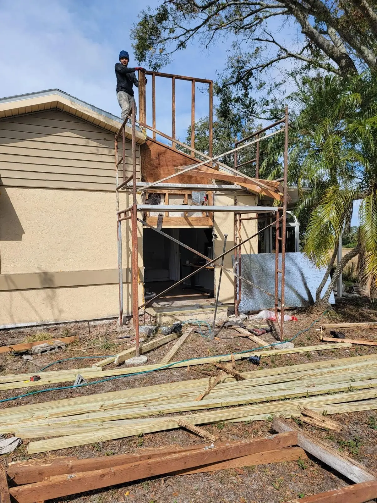 Scaffold beside a house with the chimney chase framed back up on the roof and new lumber stacked on the ground